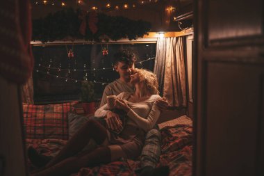 Noel 'i ve yeni yılı kutlayan mutlu çift kış tatili sezonunu karavanda kutluyor. Çay içen genç çift Xmas karavanında sarılıp öpüşüyor.