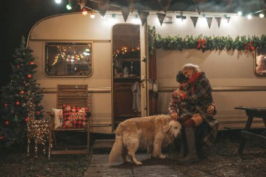 Noel 'i ve yeni yılı kutlayan mutlu çift, kış tatili sezonunu Camper Park' ta kutluyor. Genç mutlu çift, Xmas karavanı yakınında Golden Retriever köpeğiyle sarılıp vakit geçiriyorlar.