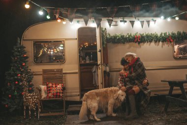 Noel 'i ve yeni yılı kutlayan mutlu çift, kış tatili sezonunu Camper Park' ta kutluyor. Genç mutlu çift, Xmas karavanı yakınında Golden Retriever köpeğiyle sarılıp vakit geçiriyorlar.
