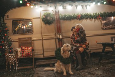 Noel 'i ve yeni yılı kutlayan mutlu çift, kış tatili sezonunu Camper Park' ta kutluyor. Genç mutlu çift, Xmas karavanı yakınında Golden Retriever köpeğiyle sarılıp vakit geçiriyorlar.