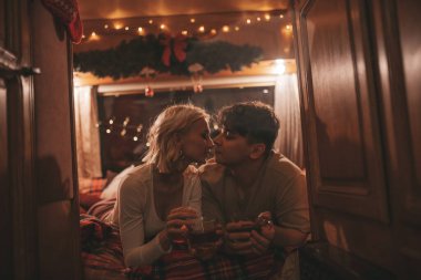 Noel 'i ve yeni yılı kutlayan mutlu çift kış tatili sezonunu karavanda kutluyor. Çay içen genç çift Xmas karavanında sarılıp öpüşüyor.