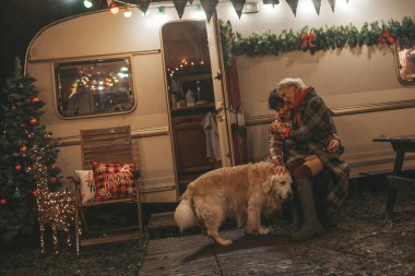 Noel 'i ve yeni yılı kutlayan mutlu çift, kış tatili sezonunu Camper Park' ta kutluyor. Genç mutlu çift, Xmas karavanı yakınında Golden Retriever köpeğiyle sarılıp vakit geçiriyorlar.