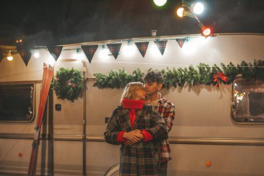 Noel 'i ve yeni yılı kutlayan mutlu çift, kış tatili sezonunu Camper Park' ta kutluyor. Genç çift dinleniyor ve rahatlıyor. Birlikte zaman geçiriyorlar. Xmas karavanı yakınında sarılıp öpüşüyorlar.