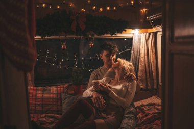 Noel 'i ve yeni yılı kutlayan mutlu çift kış tatili sezonunu karavanda kutluyor. Çay içen genç çift Xmas karavanında sarılıp öpüşüyor.