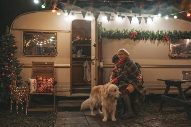 Noel 'i ve yeni yılı kutlayan mutlu çift, kış tatili sezonunu Camper Park' ta kutluyor. Genç mutlu çift, Xmas karavanı yakınında Golden Retriever köpeğiyle sarılıp vakit geçiriyorlar.