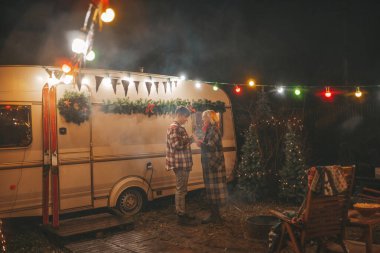 Noel 'i ve yeni yılı kutlayan mutlu çift, kış tatili sezonunu Camper Park' ta kutluyor. Genç çift dinleniyor ve rahatlıyor. Birlikte zaman geçiriyorlar. Xmas karavanı yakınında sarılıp öpüşüyorlar.