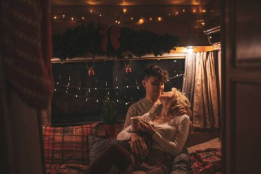 Noel 'i ve yeni yılı kutlayan mutlu çift kış tatili sezonunu karavanda kutluyor. Çay içen genç çift Xmas karavanında sarılıp öpüşüyor.