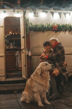 Noel 'i ve yeni yılı kutlayan mutlu çift, kış tatili sezonunu Camper Park' ta kutluyor. Genç mutlu çift, Xmas karavanı yakınında Golden Retriever köpeğiyle sarılıp vakit geçiriyorlar.