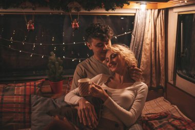 Noel 'i ve yeni yılı kutlayan mutlu çift kış tatili sezonunu karavanda kutluyor. Çay içen genç çift Xmas karavanında sarılıp öpüşüyor.