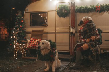 Noel 'i ve yeni yılı kutlayan mutlu çift, kış tatili sezonunu Camper Park' ta kutluyor. Genç mutlu çift, Xmas karavanı yakınında Golden Retriever köpeğiyle sarılıp vakit geçiriyorlar.