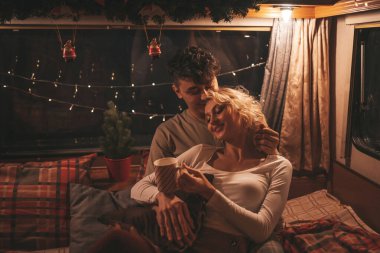 Noel 'i ve yeni yılı kutlayan mutlu çift kış tatili sezonunu karavanda kutluyor. Çay içen genç çift Xmas karavanında sarılıp öpüşüyor.