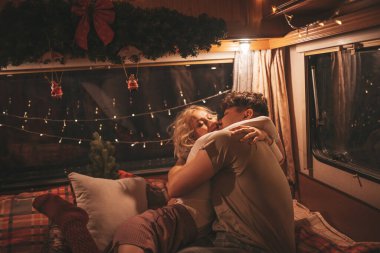 Noel 'i ve yeni yılı kutlayan mutlu çift kış tatili sezonunu karavanda kutluyor. Çay içen genç çift Xmas karavanında sarılıp öpüşüyor.