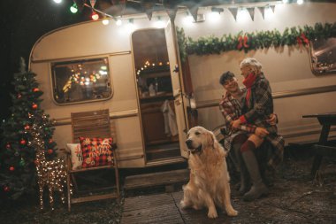 Noel 'i ve yeni yılı kutlayan mutlu çift, kış tatili sezonunu Camper Park' ta kutluyor. Genç mutlu çift, Xmas karavanı yakınında Golden Retriever köpeğiyle sarılıp vakit geçiriyorlar.