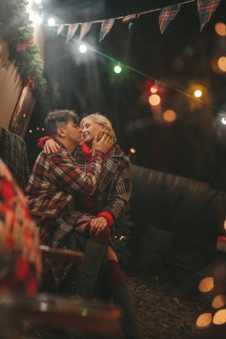 Noel 'i ve yeni yılı kutlayan mutlu çift, kış tatili sezonunu Camper Park' ta kutluyor. Genç çift dinleniyor ve rahatlıyor. Birlikte zaman geçiriyorlar. Xmas karavanı yakınında sarılıp öpüşüyorlar.