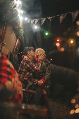 Noel 'i ve yeni yılı kutlayan mutlu çift, kış tatili sezonunu Camper Park' ta kutluyor. Genç çift dinleniyor ve rahatlıyor. Birlikte zaman geçiriyorlar. Xmas karavanı yakınında sarılıp öpüşüyorlar.