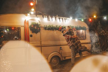 Noel 'i ve yeni yılı kutlayan mutlu çift, kış tatili sezonunu Camper Park' ta kutluyor. Genç çift dinleniyor ve rahatlıyor. Birlikte zaman geçiriyorlar. Xmas karavanı yakınında sarılıp öpüşüyorlar.