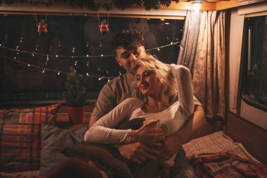 Noel 'i ve yeni yılı kutlayan mutlu çift kış tatili sezonunu karavanda kutluyor. Çay içen genç çift Xmas karavanında sarılıp öpüşüyor.