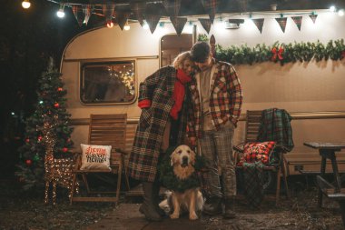 Noel 'i ve yeni yılı kutlayan mutlu çift, kış tatili sezonunu Camper Park' ta kutluyor. Genç mutlu çift, Xmas karavanı yakınında Golden Retriever köpeğiyle sarılıp vakit geçiriyorlar.