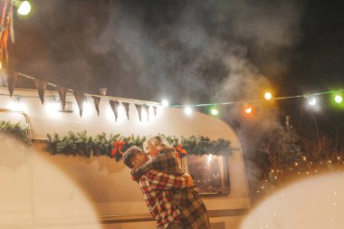 Noel 'i ve yeni yılı kutlayan mutlu çift, kış tatili sezonunu Camper Park' ta kutluyor. Genç çift dinleniyor ve rahatlıyor. Birlikte zaman geçiriyorlar. Xmas karavanı yakınında sarılıp öpüşüyorlar.