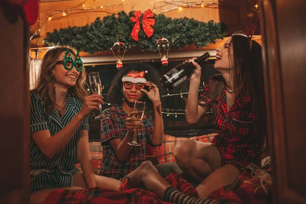 快乐的女孩们在营地庆祝圣诞节和新年假期 活跃的 多样化的年轻女性快乐地拥抱在一起 在旧式的圣诞预告片里畅饮起泡的葡萄酒 — 图库照片