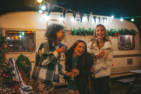快乐的女孩们在户外庆祝圣诞节和新年假期 年轻而多样化的女性快乐的女性朋友在旧式的圣诞预告片旁畅饮起泡的美酒 — 图库照片