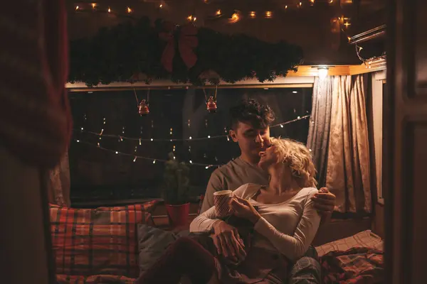 Noel 'i ve yeni yılı kutlayan mutlu çift kış tatili sezonunu karavanda kutluyor. Çay içen genç çift Xmas karavanında sarılıp öpüşüyor.