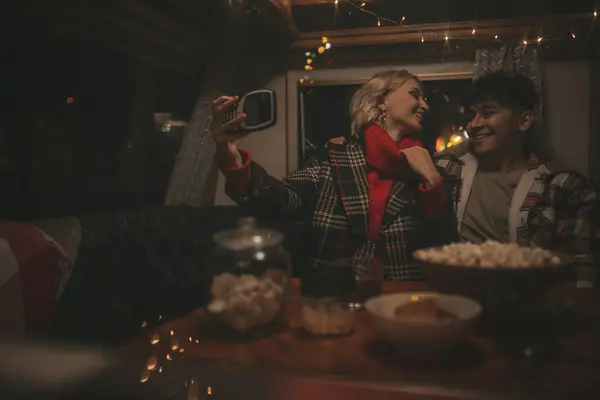 Happy couple celebrating Christmas and New Year winter holidays season in Camper Park. Young couple spending time together take selfie photo for social media in Xmas camper trailer