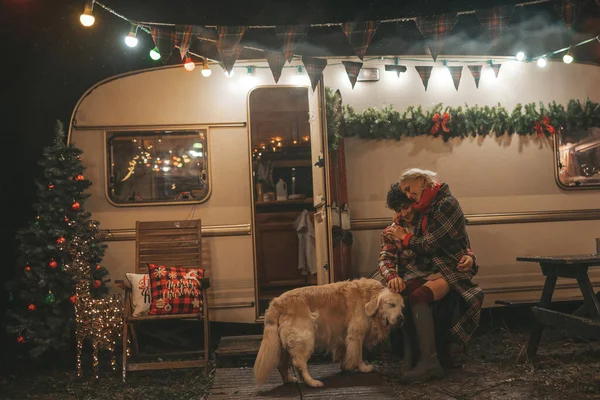 在坎普公园 一对欢欢喜喜的夫妇在庆祝圣诞节和新年假期 一对快乐的年轻夫妇在耶诞露营拖车旁拥抱 与金毛猎犬共度时光 — 图库照片