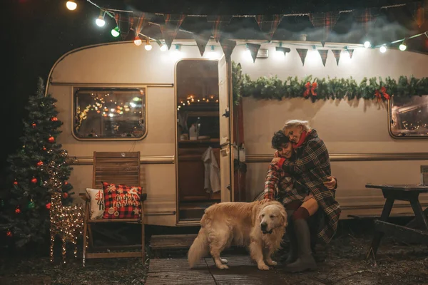 キャンパーパークでクリスマスと新年の冬の休暇シーズンを祝うハッピーカップル 若い喜びのカップルは Xmasキャンピングカーのトレーラーの近くでゴールデンレトリーバー犬と一緒に抱擁し 時間を過ごしました — ストック写真