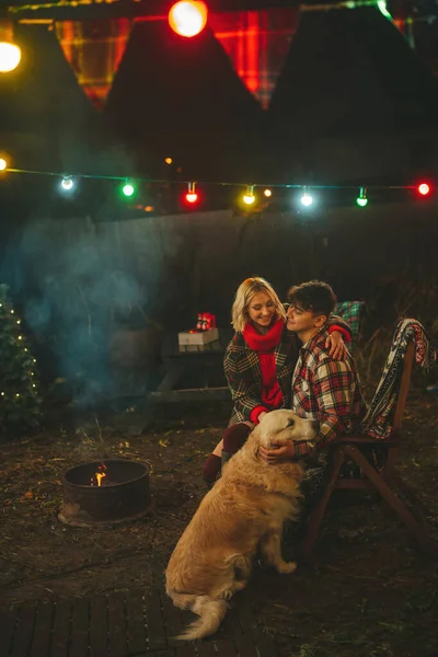 キャンパーパークでクリスマスと新年の冬の休暇シーズンを祝うハッピーカップル 若い喜びのカップルは Xmasキャンピングカーのトレーラーの近くでゴールデンレトリーバー犬と一緒に抱擁し 時間を過ごしました — ストック写真