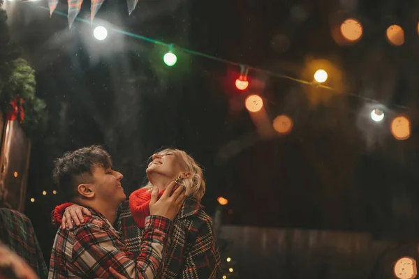 Happy couple celebrating Christmas and New Year winter holidays season in Camper Park. Young couple rest and relaxation spending time together hugs and kisses near Xmas camper trailer