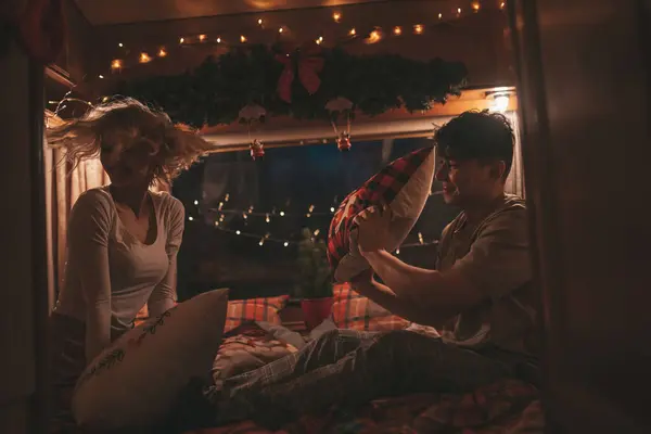 キャンパーでクリスマスと新年の冬の休暇シーズンを祝うハッピーカップル 若いカップル楽しい時間を一緒に過ごすXmasキャンパーのトレーラーで楽しい枕の戦い — ストック写真