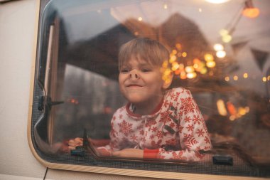 Küçük çocuk Noel 'i ve yeni yıl tatilini kutlarken yüzünü buruşturuyor Noel Baba' yı Noel kampı karavanında bekliyor.
