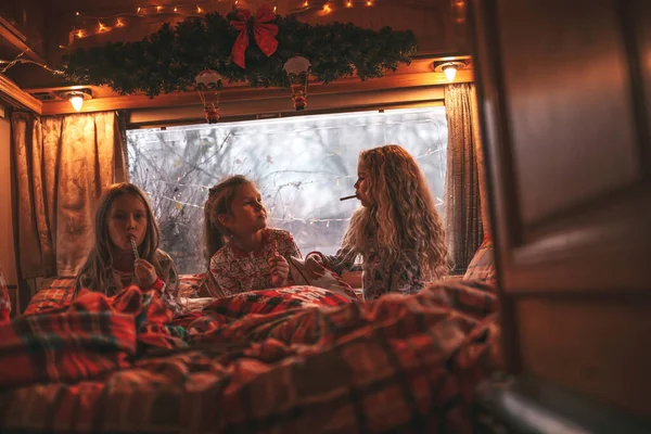 キャンパーでクリスマスと新年の冬の休暇シーズンを祝う子供たち 小さな女の子は子供の頃を楽しんでいるXmasキャンパーのトレーラーで耳元で秘密をささやく笑顔の時間を一緒に過ごします ストック写真