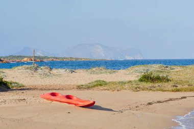 Kumsalda kırmızı bir kano resmi.