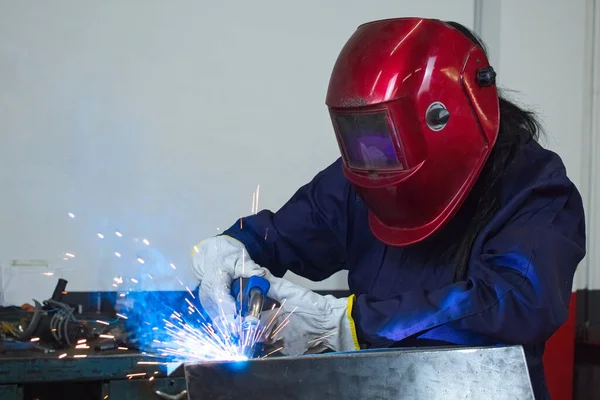woman with gloves welding metal with protection mask and overalls