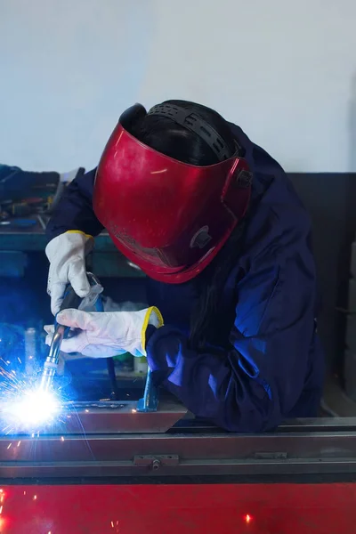 worker woman with gloves working in a workshop welding metal with protection mask and overalls