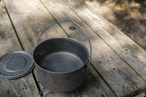 A titanium pot for making food on a gas stove on a camping wooden table in the forest. High quality photo