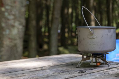 A titanium pot for making food on a gas stove on a camping wooden table in the forest. High quality photo
