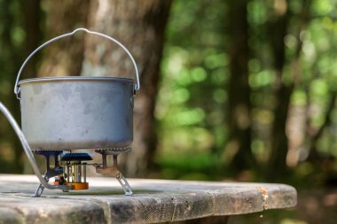 A titanium pot for making food on a gas stove on a camping wooden table in the forest. High quality photo