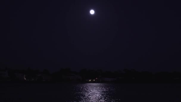 暗い夜空の満月で 海岸沿いの住宅の上の水に反射する星はありません — ストック動画