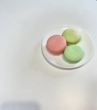 photo captures the essence of delicate and delicious macarons. The photo features a selection of pink and green macarons artfully arranged on a plate, creating a visually stunning composition that is perfect for a variety of creative projects. 