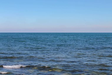 Gökyüzünün arka planında beyaz köpük ve dalgalarla mavi su ve deniz