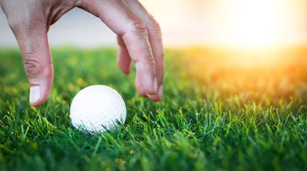 Golfer's hand holds golf ball close up on tee grass on blurred beautiful landscape of green background. Concept international sport that rely on precision skills for health relaxation.