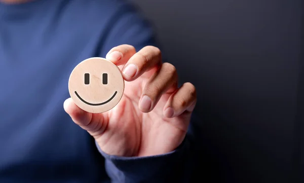 A wooden block with a smiley face symbol on the hand of a customer who uses the service, rating, rating, customer experience, satisfaction and the best service scoring concept.