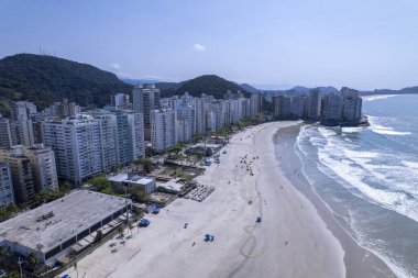 Bu kıyı manzarasında Guaruja, Sao Paulo 'daki Praia da Pitangueiras, açık mavi suların altın kumlarla buluştuğu ve kıyı boyunca uzanan yüksek binalar ziyaretçileri plajın tadını çıkarmaya davet ediyor..