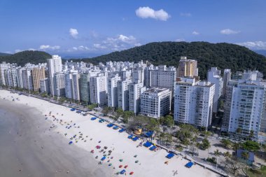 Bu kıyı manzarasında Guaruja, Sao Paulo 'daki Praia da Pitangueiras, açık mavi suların altın kumlarla buluştuğu ve kıyı boyunca uzanan yüksek binalar ziyaretçileri plajın tadını çıkarmaya davet ediyor..