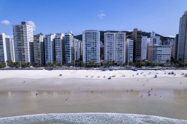 Bu kıyı manzarasında Guaruja, Sao Paulo 'daki Praia da Pitangueiras, açık mavi suların altın kumlarla buluştuğu ve kıyı boyunca uzanan yüksek binalar ziyaretçileri plajın tadını çıkarmaya davet ediyor..