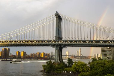 Kısa bir yağmurun ardından New York 'taki Manhattan Köprüsü' nün üzerinde bir gökkuşağı güzellikle uzanır, yakınlardaki binalarla ve aşağıdaki nehirle çelişir..