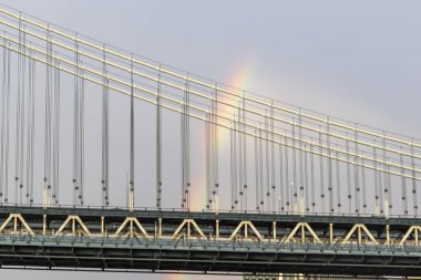 Kısa bir yağmurun ardından New York 'taki Manhattan Köprüsü' nün üzerinde bir gökkuşağı güzellikle uzanır, yakınlardaki binalarla ve aşağıdaki nehirle çelişir..